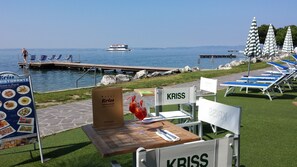 Ein Essbereich mit Meerblick, ein Boot im Hintergrund und Liegestühle am Wasser.