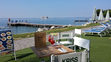 Un comedor con vistas al mar, un barco al fondo y sillones de descanso a la orilla.