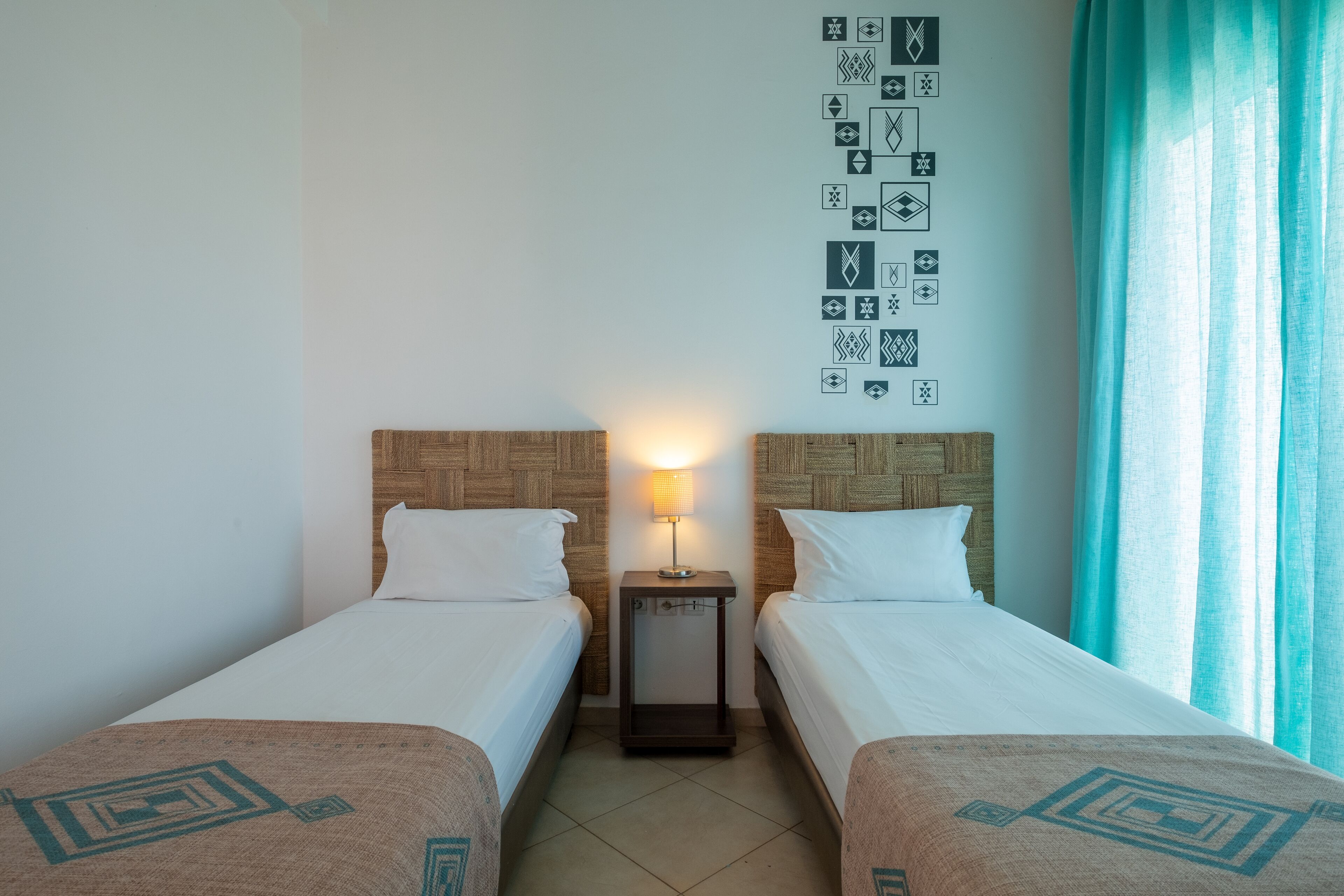 A hotel room with two beds, a nightstand with a lamp, and a wall decorated with geometric patterns.