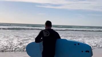Una persona caminando sobre la playa llevando una tabla de surf.