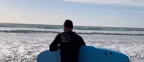 Una persona caminando sobre la playa llevando una tabla de surf.
