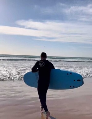A person walking on a beach carrying a surfboard. - Lunja Village Taghazout (Tamri)