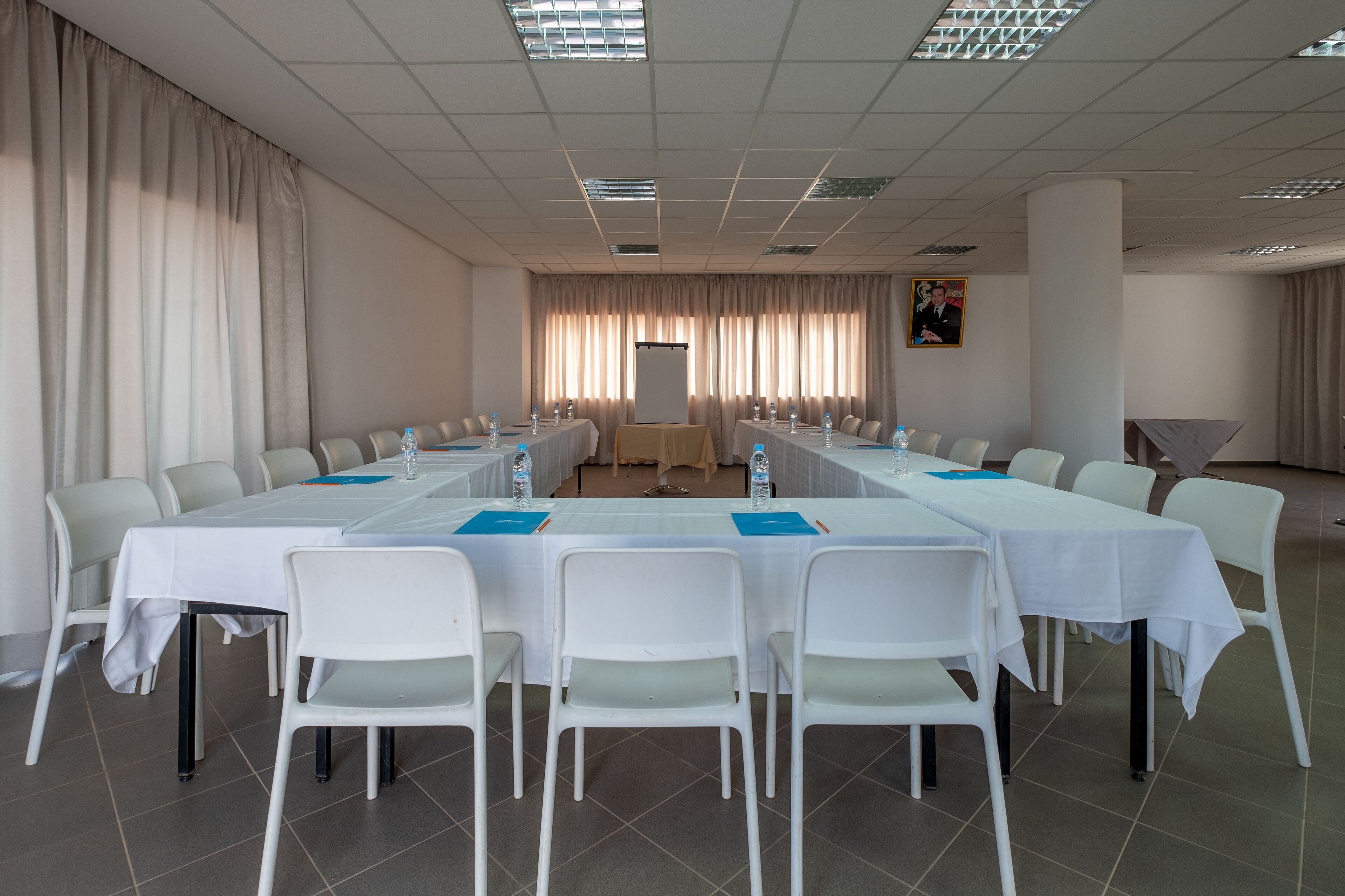 Una sala conferenze con un lungo tavolo, sedie bianche e uno schermo per proiezioni.