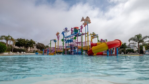 A water park with various play structures and slides over a pool. - Lunja Village Taghazout (Tamri)