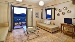 A living room with a glass coffee table, a sofa, a TV stand, and a balcony with a table and chairs. - Niriides Apartments (Igoumenitsa)