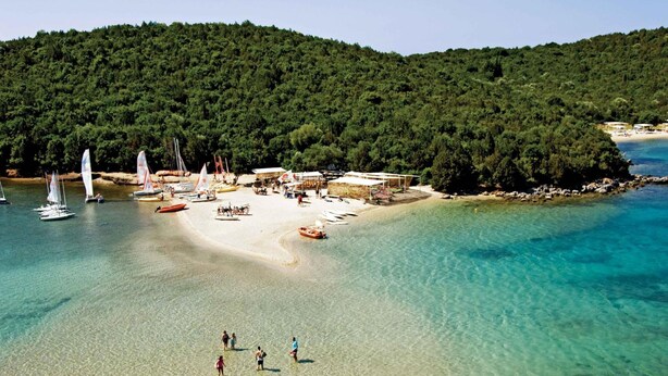 A beach with clear turquoise water, a sandy shore, and a forested hill in the background. - Niriides Apartments (Igoumenitsa)