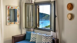 A bedroom with a bed, a window with curtains, a mirror, and two hats on the wall. - Niriides Apartments (Igoumenitsa)