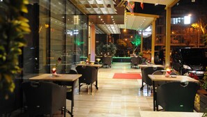 An indoor dining area with tables and chairs, a glass wall, and a red carpet. - Golden Deluxe Hotel (Adana)