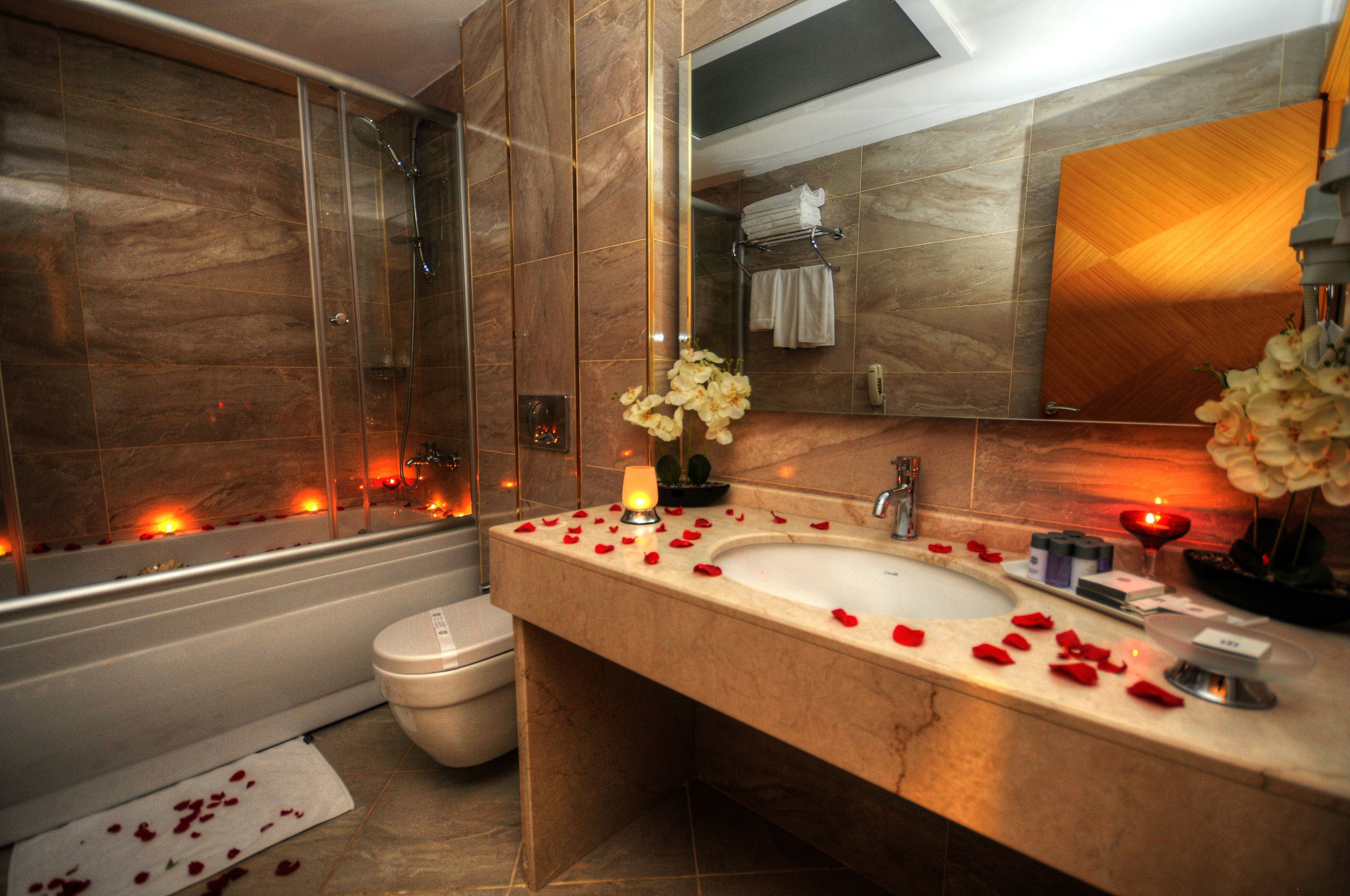 A modern bathroom with a bathtub, a toilet, and a sink with rose petals scattered on the counter.