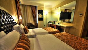 A hotel room with two beds, a desk, a chair, a television, and a mirror. - Golden Deluxe Hotel (Adana)