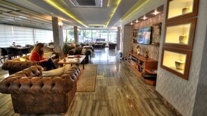 A spacious hotel lobby with leather sofas, a coffee table, and a TV mounted on the wall. - Golden Deluxe Hotel (Adana)