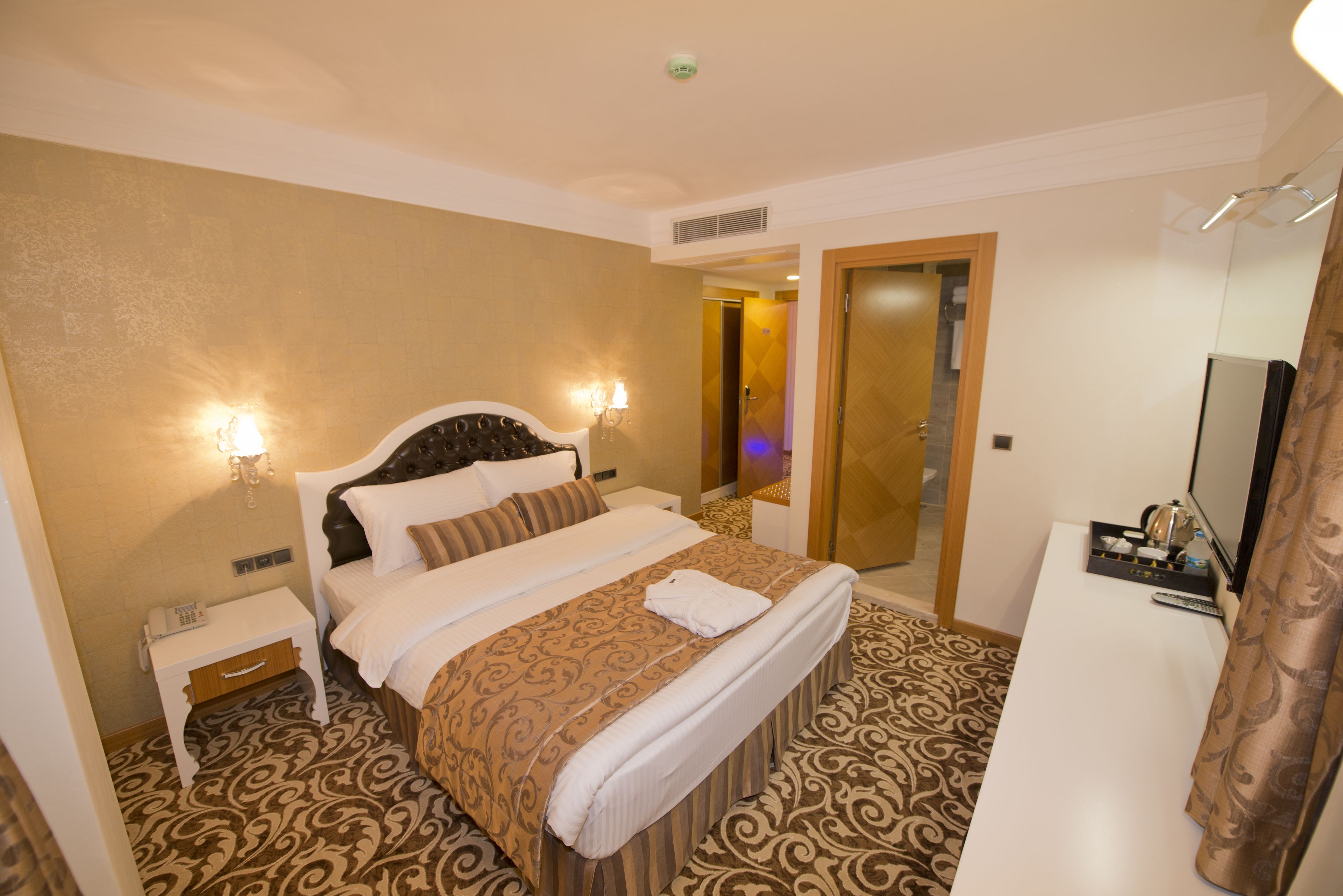 A hotel room with a bed, bedside table, and a desk with a television.