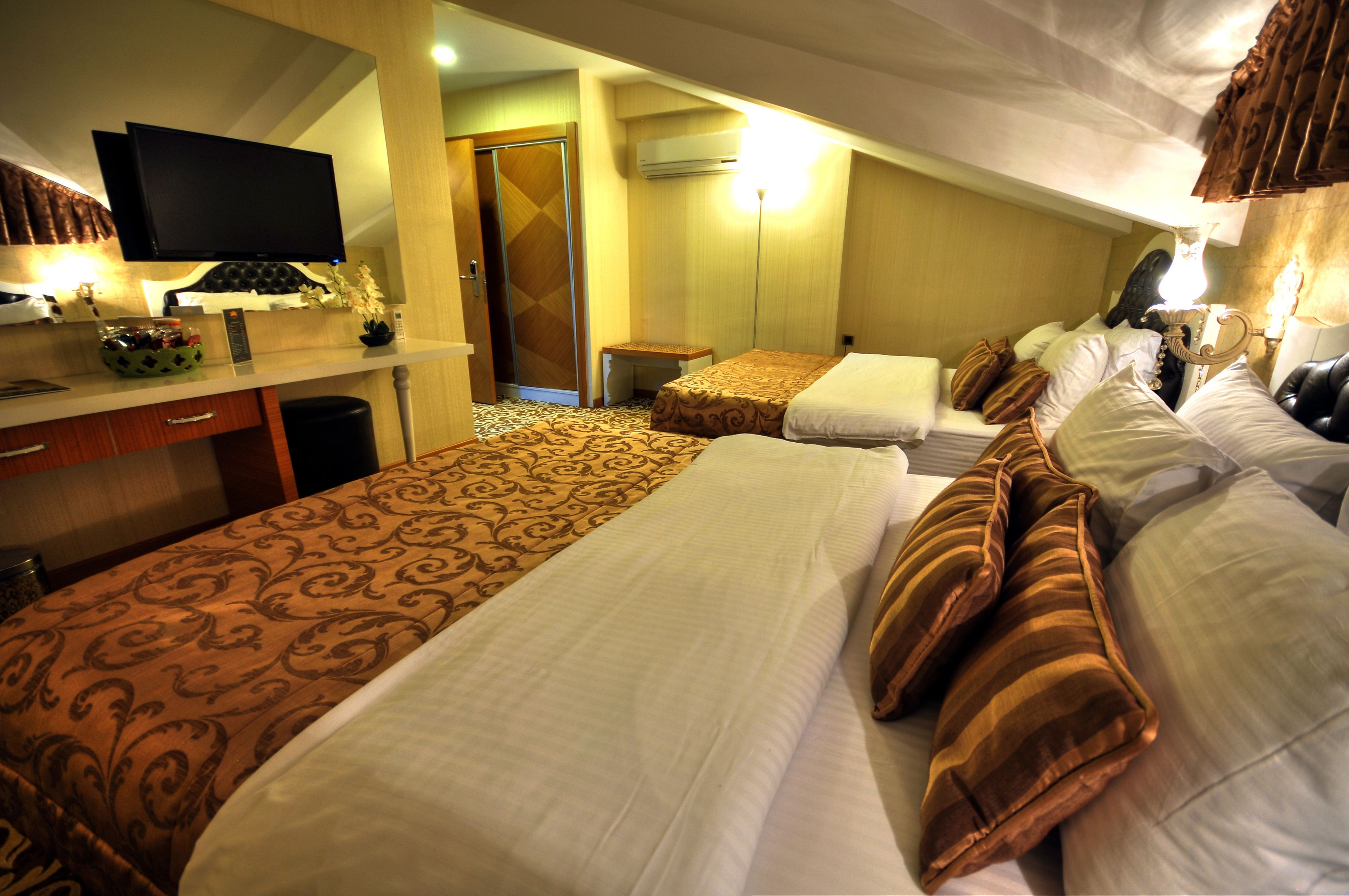 A hotel room with a large bed, a desk with a computer, a television, and an air conditioning unit.