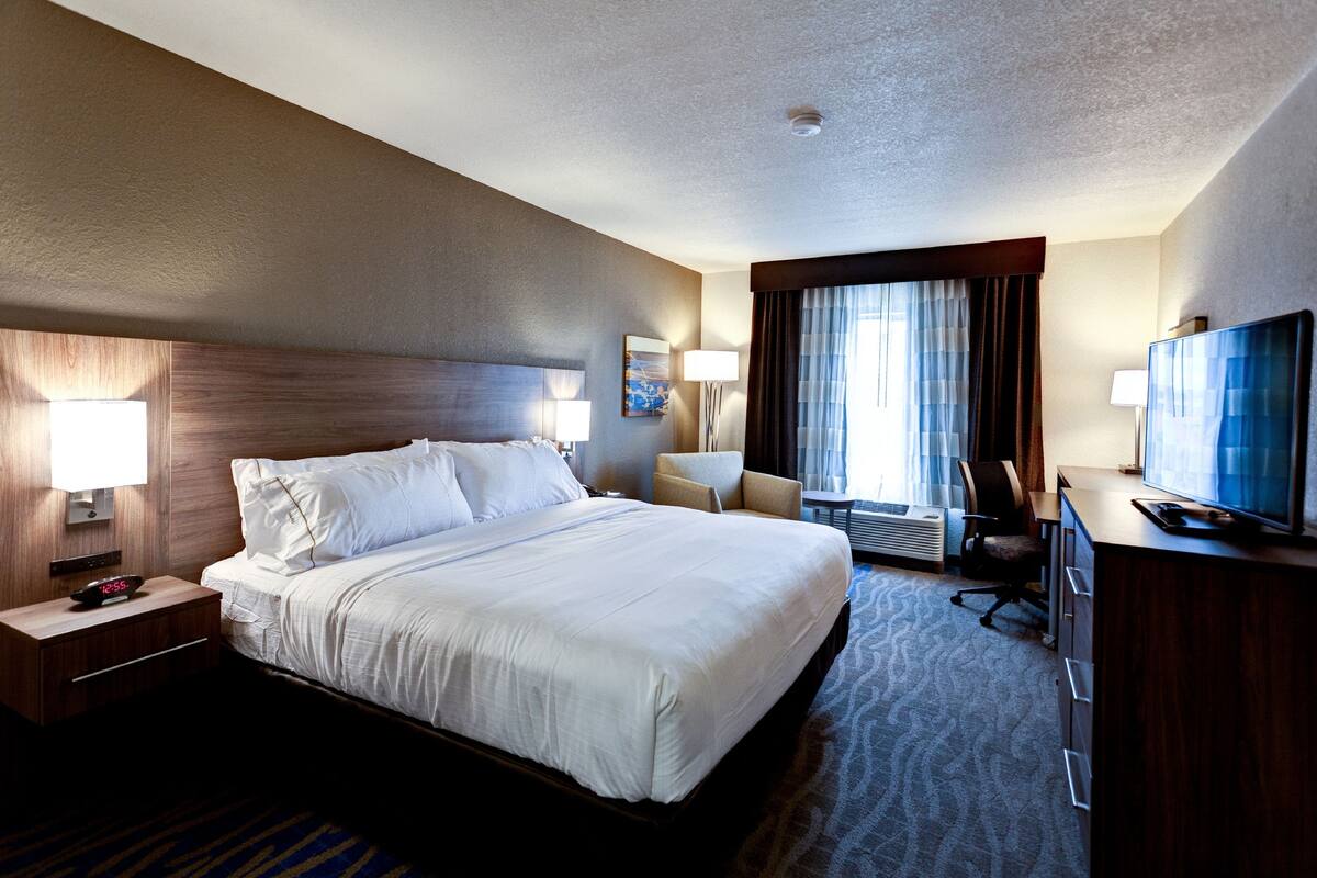 A hotel room with a large bed, a desk with a television, a chair, and a desk lamp.