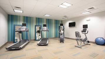 A fitness room with treadmills, an elliptical, a stationary bike, and a blue exercise ball.