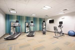 Un gimnasio con cintas de correr, una elíptica, una bicicleta estática y una pelota de ejercicios azul.
