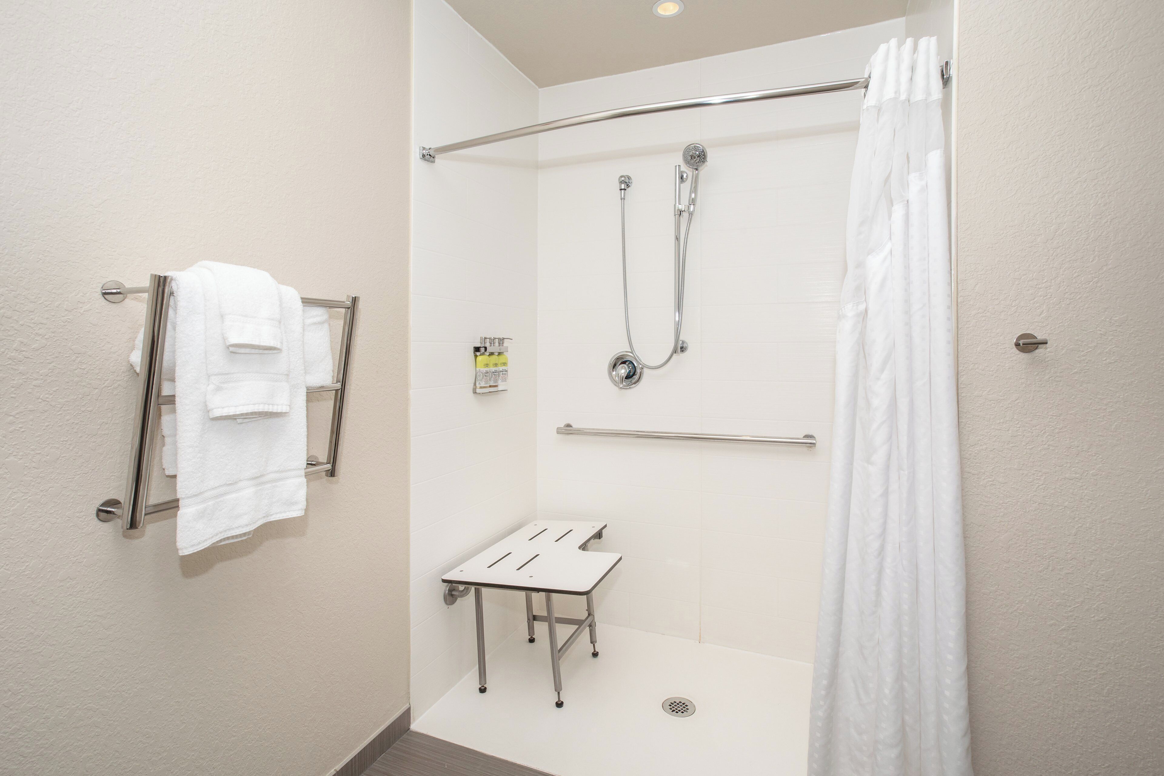 Ein modernes Badezimmer mit barrierefreier Dusche, einer Glaskabine für die Toilette und einem Handtuchhalter mit mehreren Handtüchern.