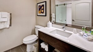 A modern bathroom with a white sink, a large mirror, a framed artwork on the wall, and a toilet. - Holiday Inn Express & Suites Manhattan by IHG (Manhattan)