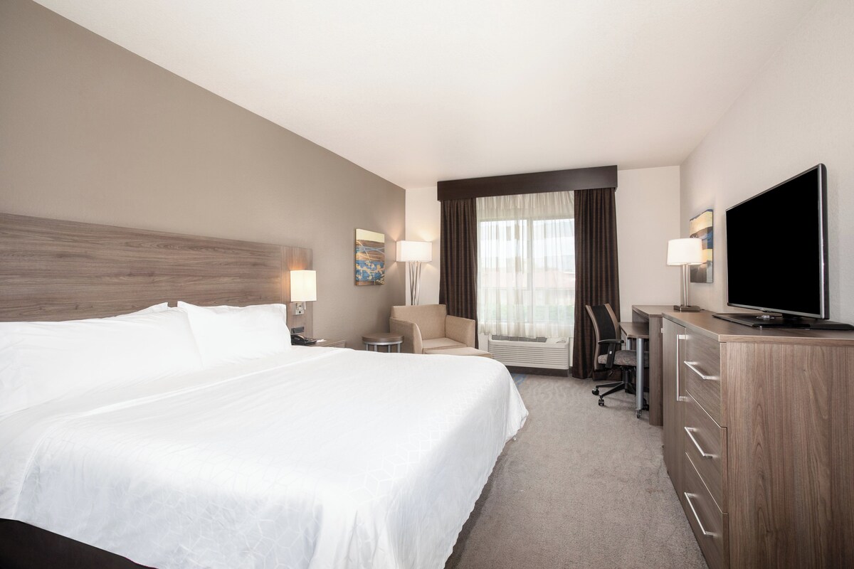Ein Hotelzimmer mit einem großen Bett, einem Schreibtisch, einem Fernseher und einem Sessel.