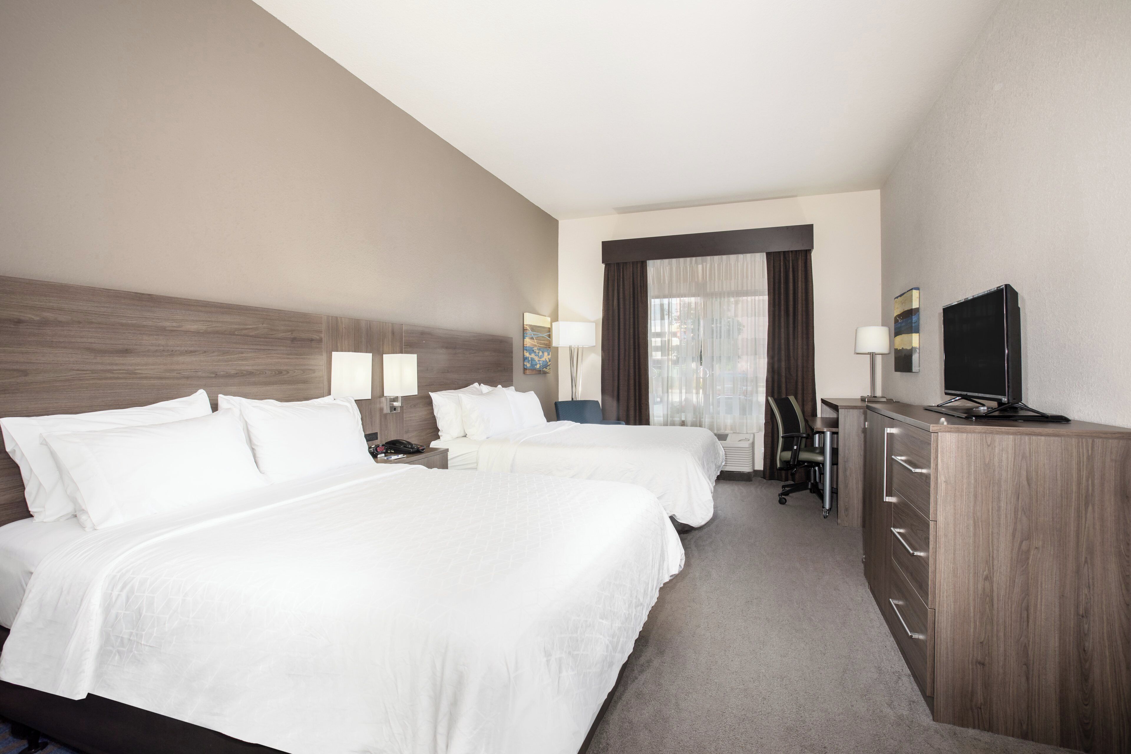 A hotel room with two beds, a desk, a chair, a television, and a dresser.
