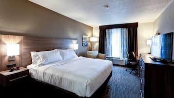 A hotel room with a large bed, a desk with a television, a chair, and a lamp.