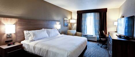 A hotel room with a large bed, a desk with a television, a chair, and a lamp.