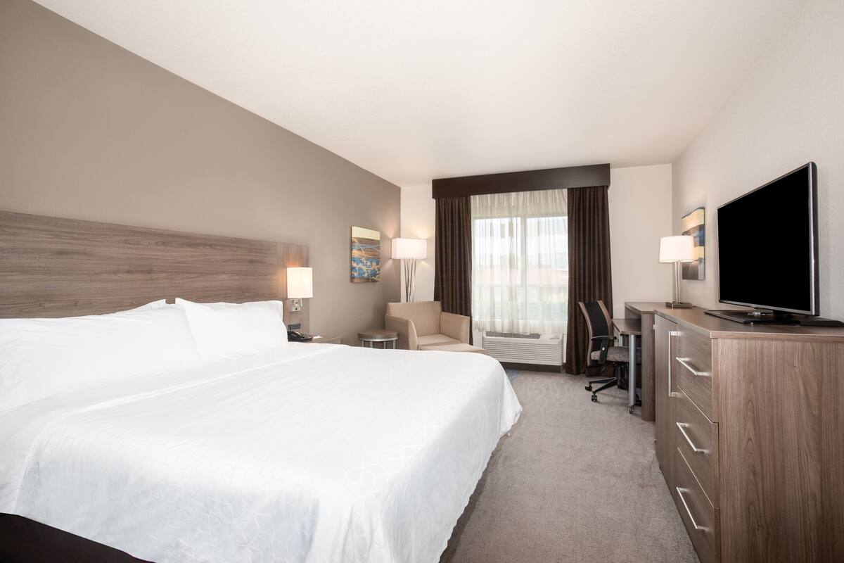 A hotel room with a large bed, a desk, a chair, a television, and a window with curtains.