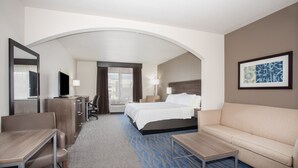 A hotel room with a bed, a sofa, a desk, a chair, a TV, and a framed picture on the wall. - Holiday Inn Express & Suites Manhattan by IHG (Manhattan)