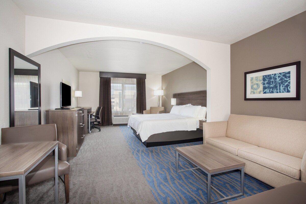 Ein Hotelzimmer mit Bett, Schreibtisch, Sessel, Sofa, Fernseher und einem gerahmten Bild an der Wand.