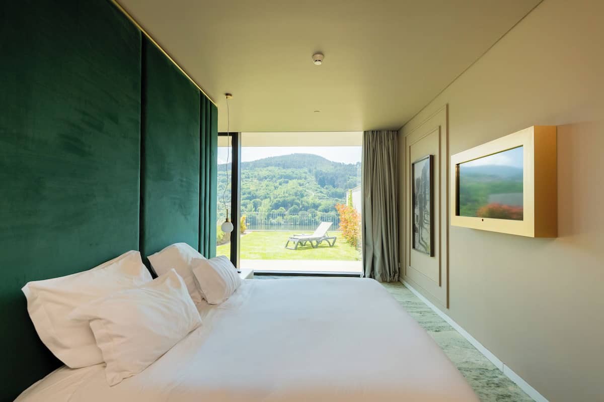 Une chambre avec un grand lit, une vue sur un jardin et un tableau encadré au mur.