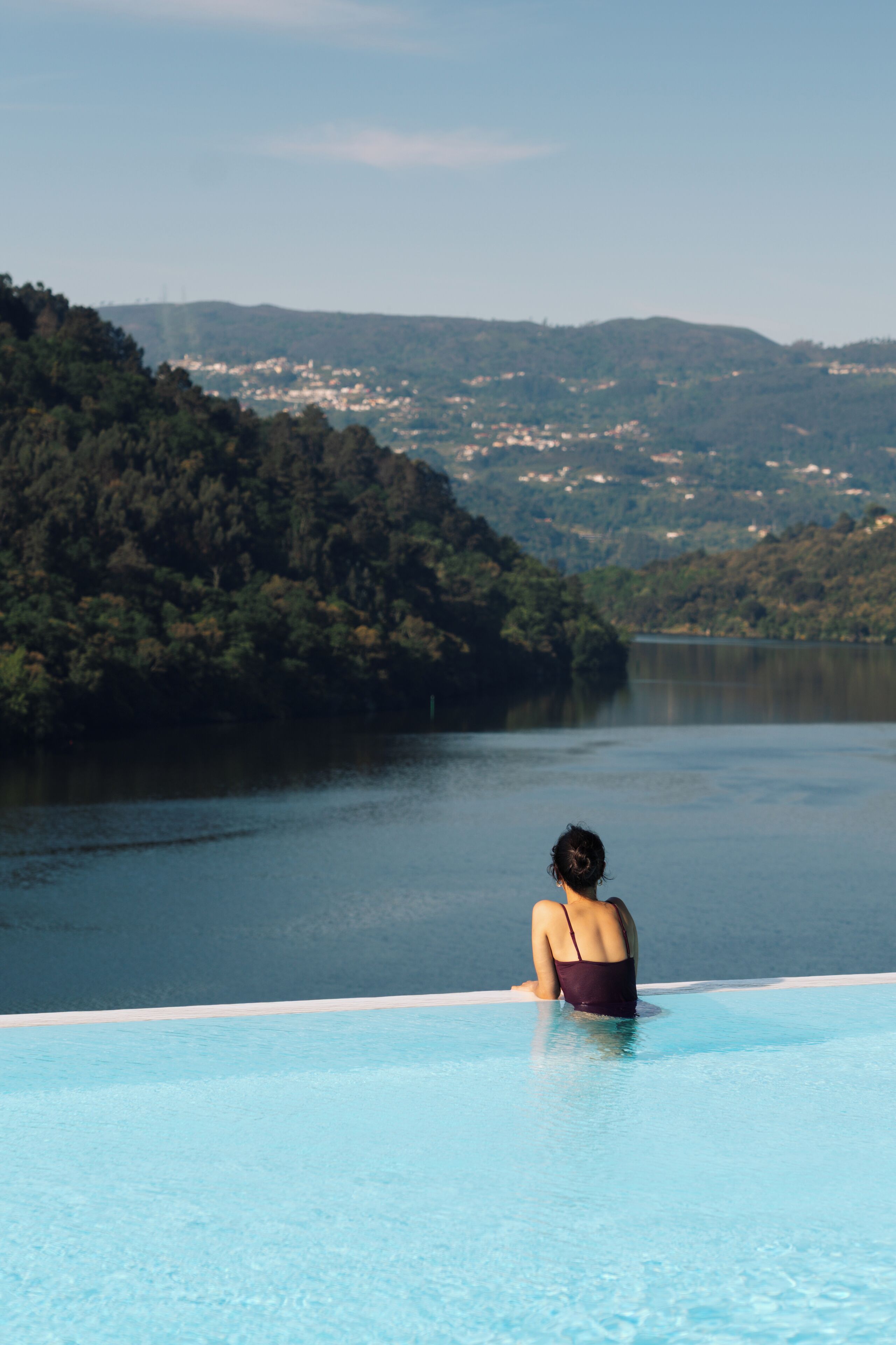 A person sitting in a pool with a view of a lake and hills.