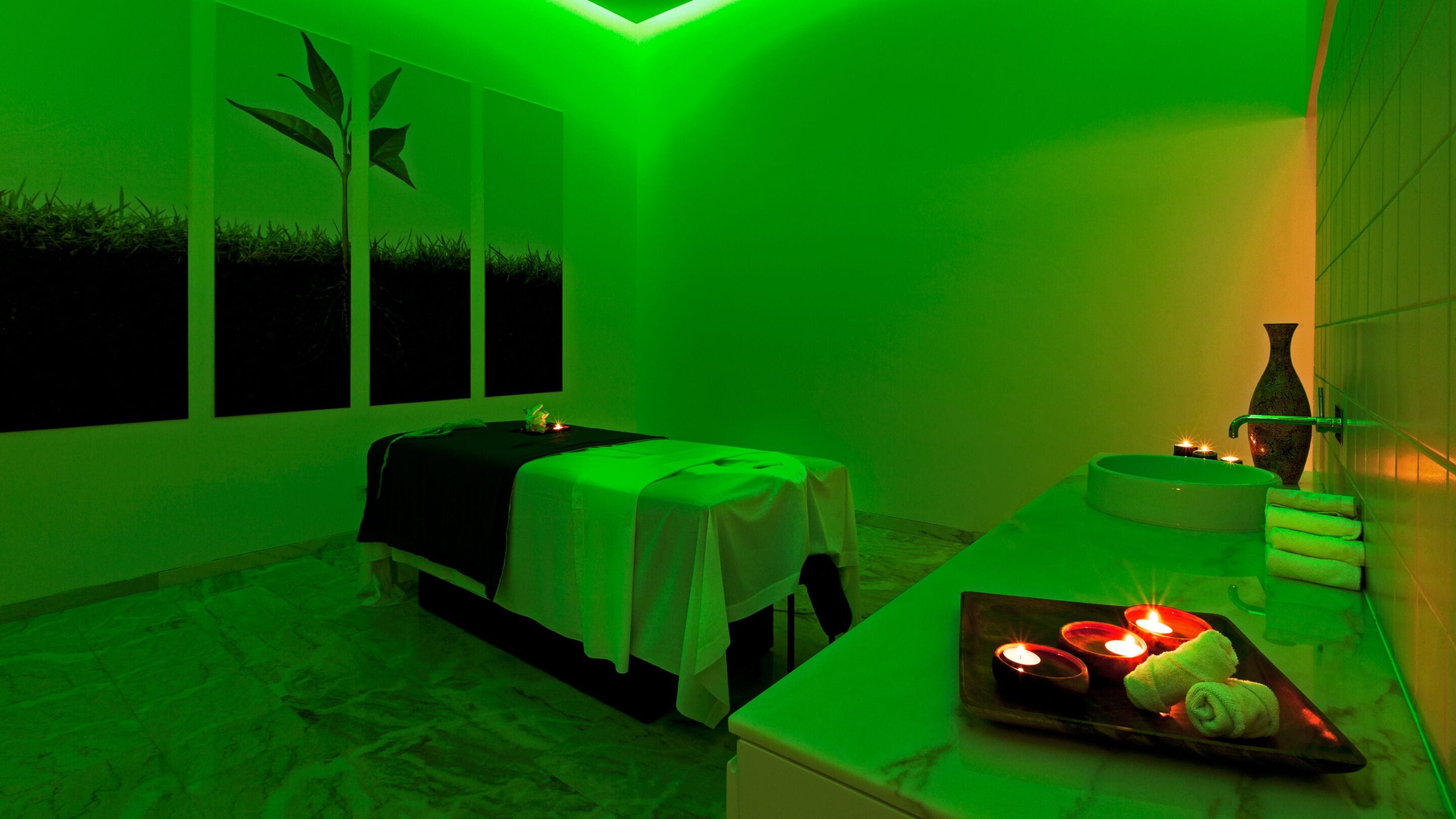 Un cuarto de spa con una camilla de masaje, una mesita con velas y un florero en la encimera.