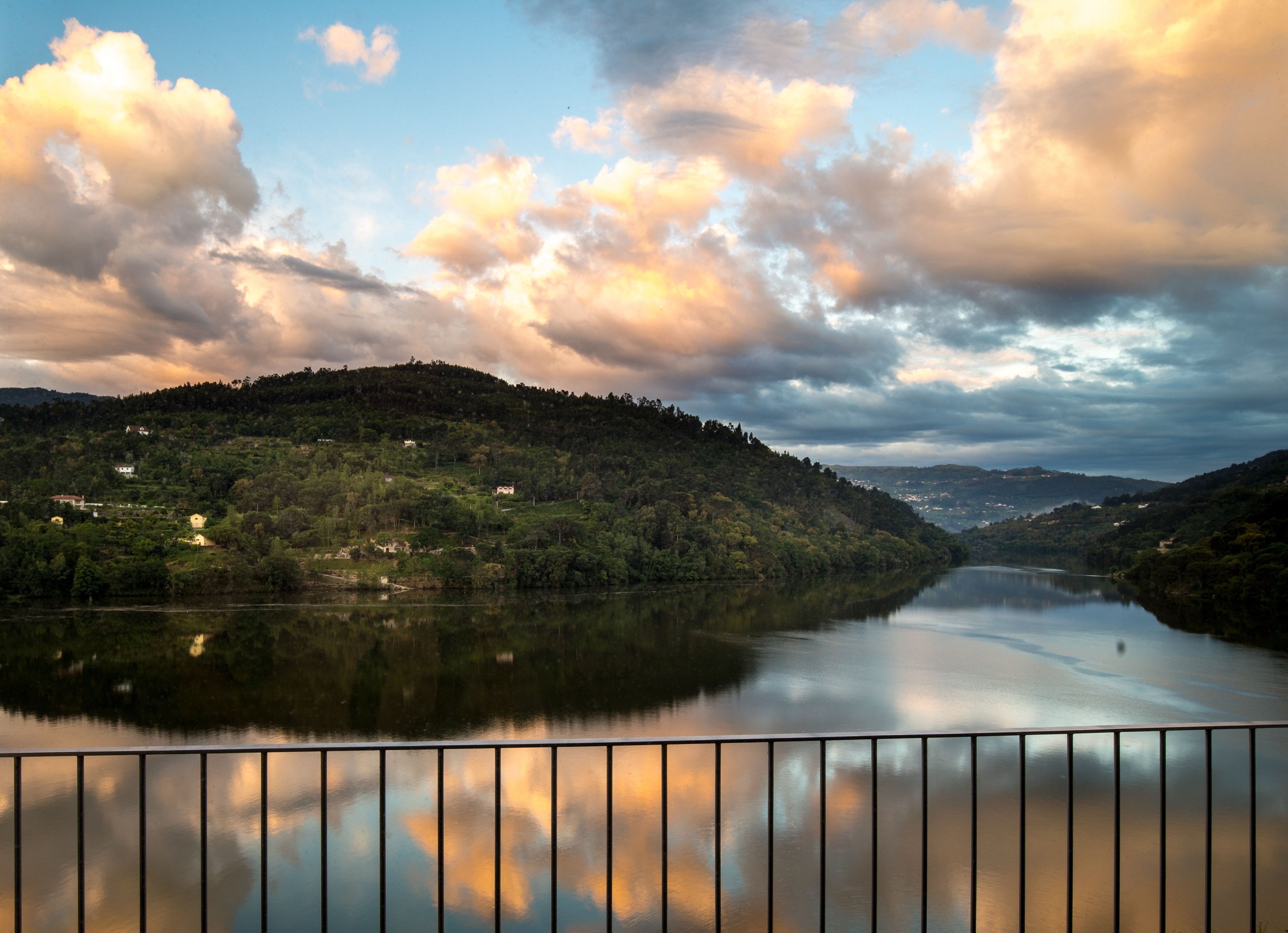 A calm river with a bridge in the foreground and hills in the background.