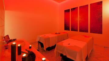 A room with two beds, a massage table, and a wall with abstract art.