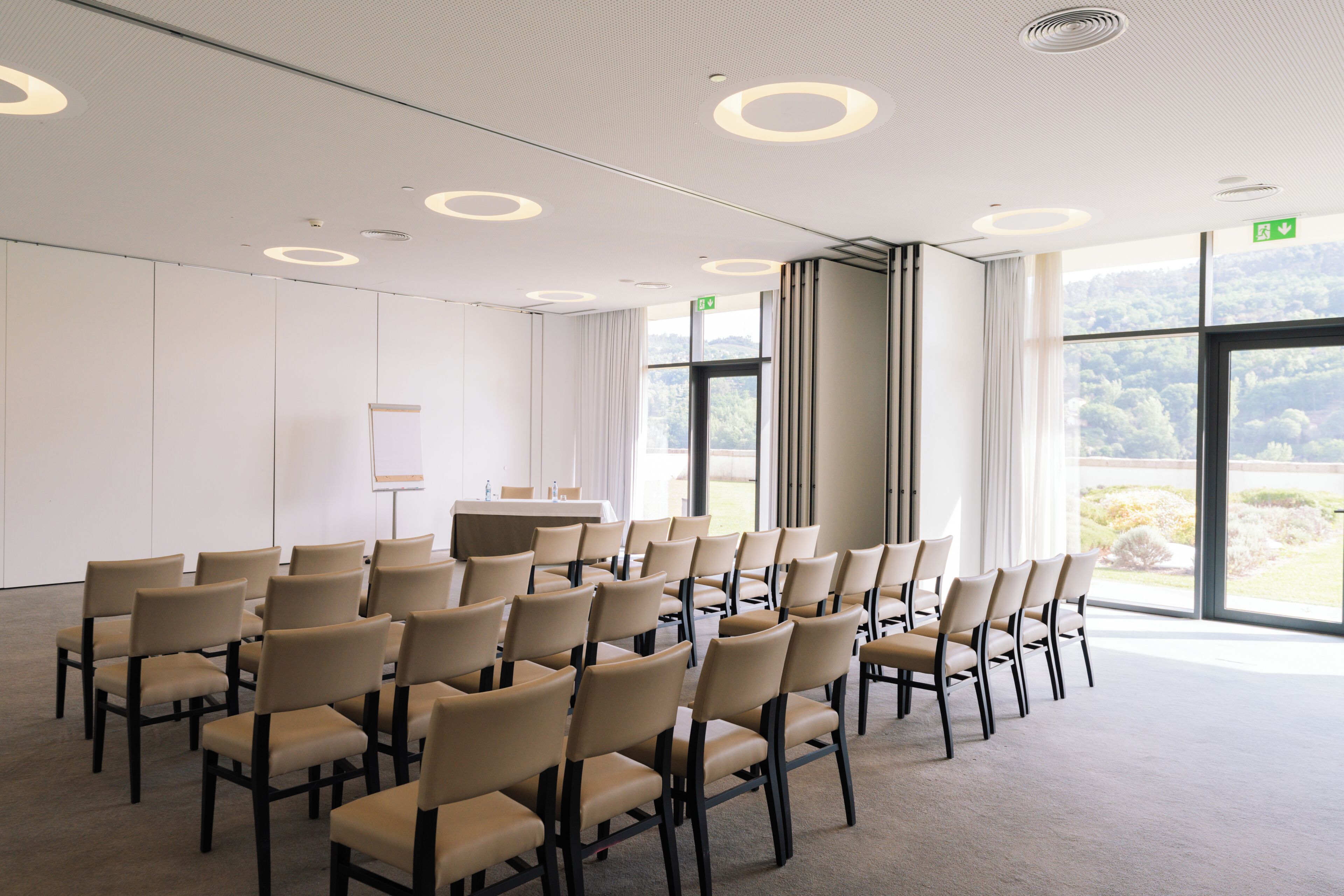 A conference room with rows of chairs, a table, and large windows with a view.