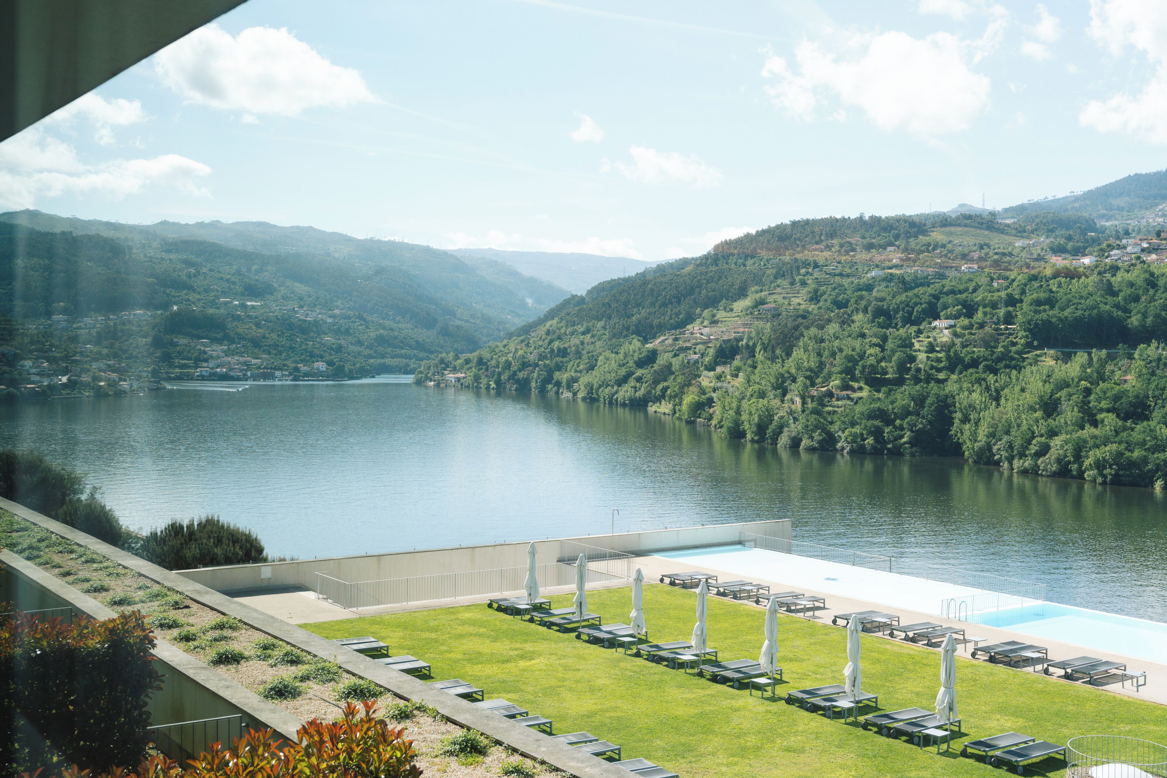 Une vue sur un lac avec des montagnes en arrière-plan, une piscine avec des chaises longues et une zone herbeuse.