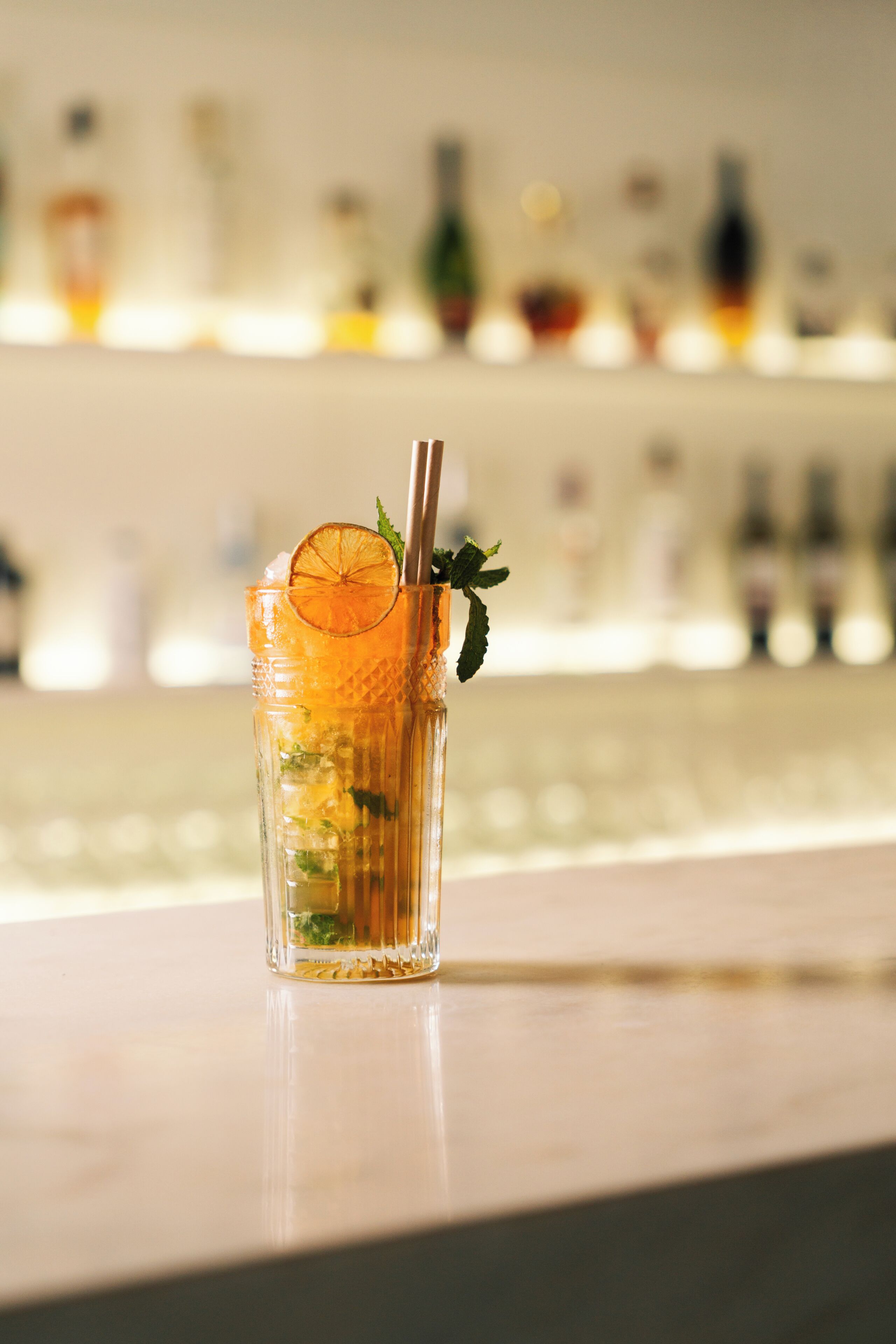 Un vaso transparente con una pajita y una rodaja de naranja sobre una barra.