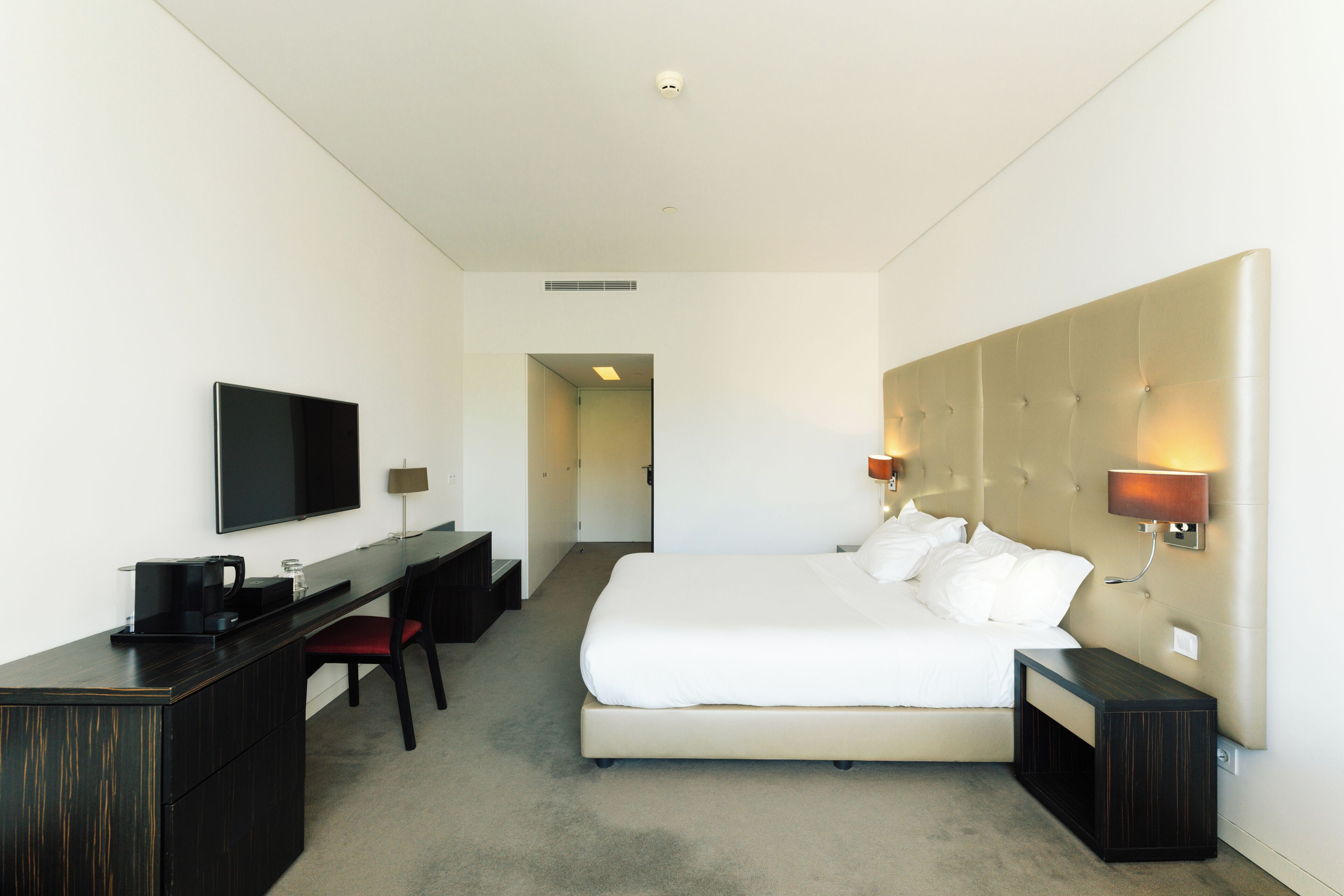 Een hotelkamer met een bed, een bureau, een stoel, een televisie en een bedlampje.