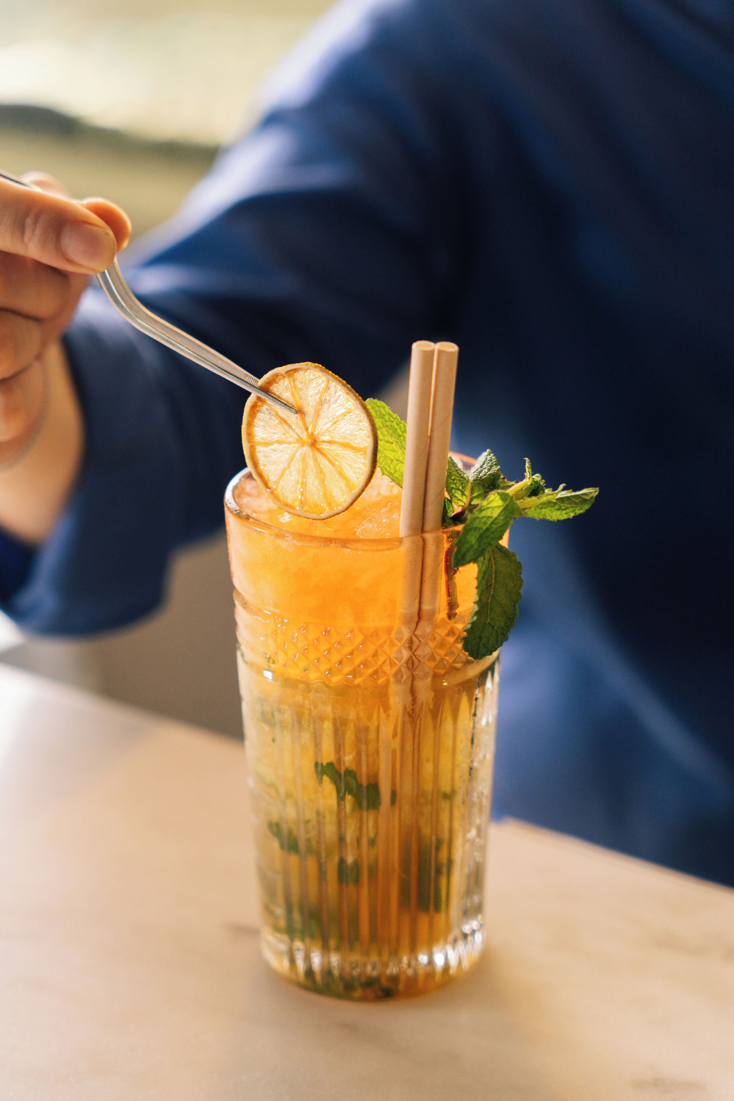 Un vaso con pajita, una rodaja de naranja y hojas de menta.