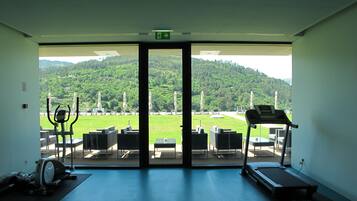 A gym with exercise equipment and a large glass door leading to an outdoor area with a view of a green landscape and hills.