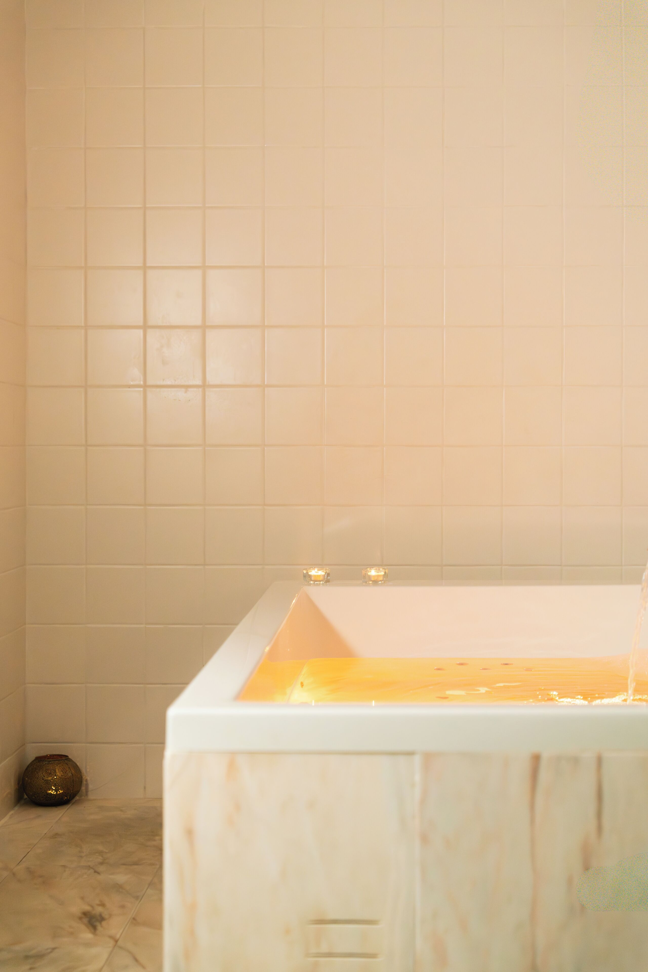 Un baño con bañera, un pequeño jarrón decorativo y una pared con azulejos.