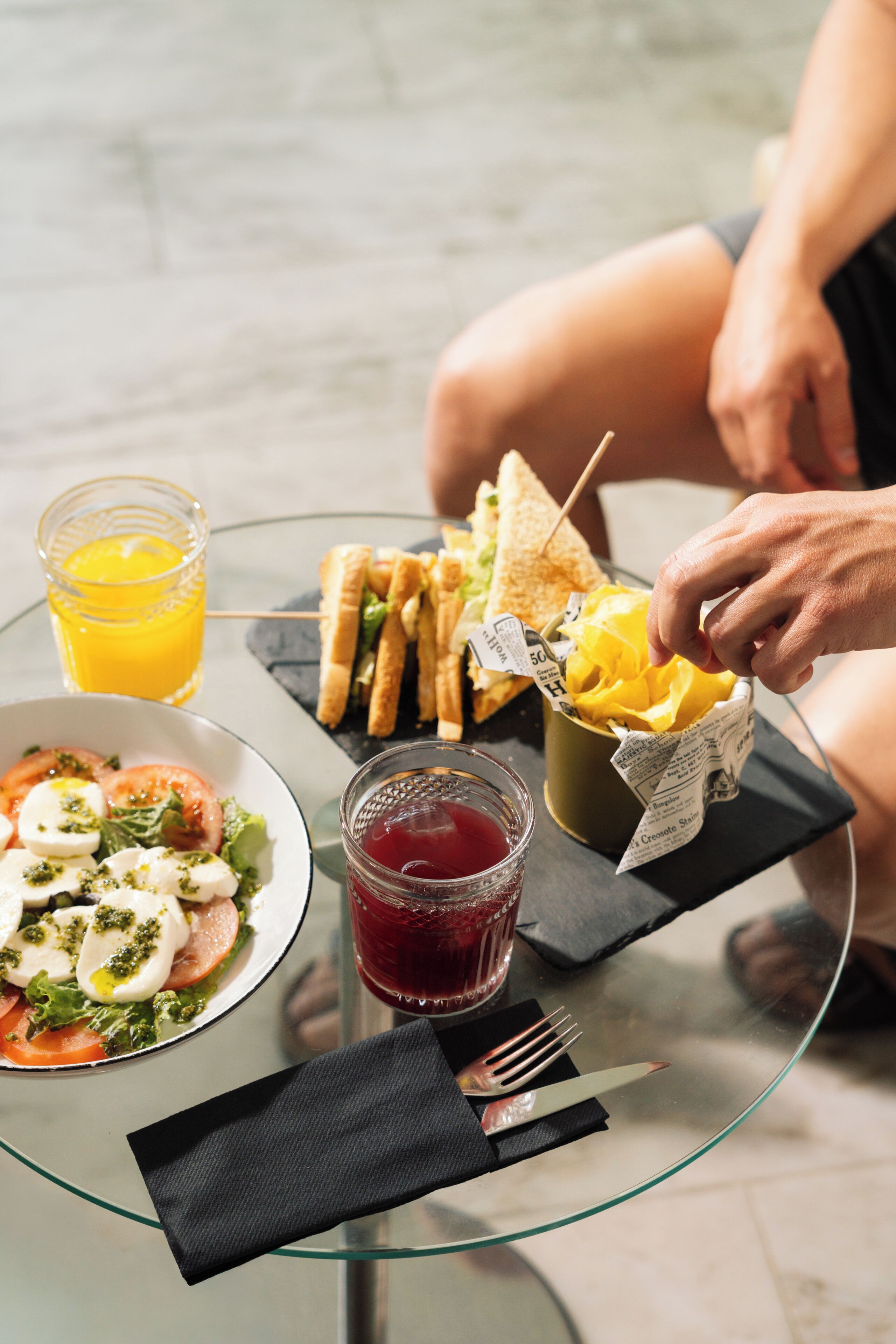 Een maaltijd met salade, een belegd broodje, friet en drankjes op een glazen tafel.