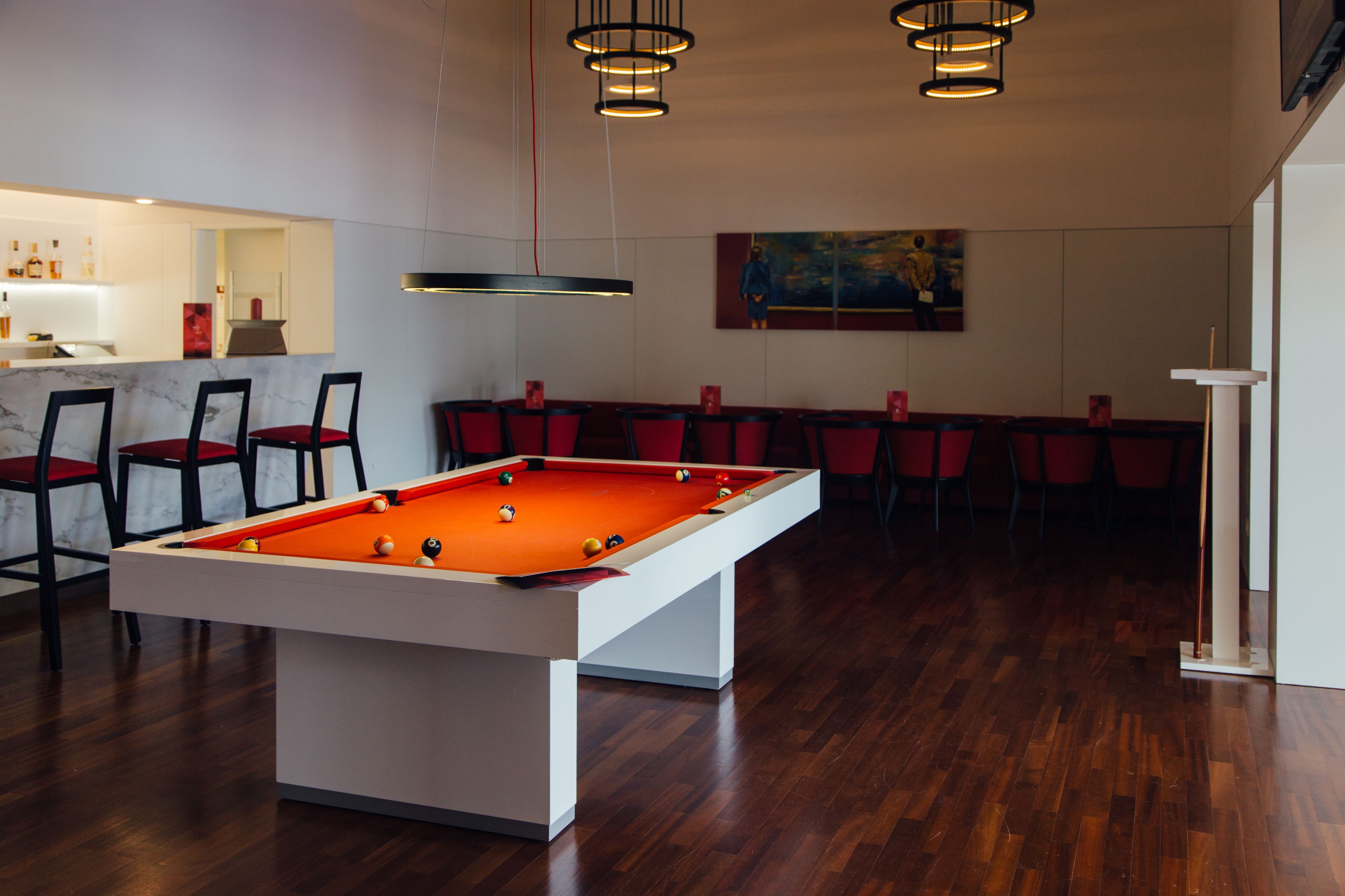 Une table de billard avec des chaises rouges, un coin bar et un tableau accroché au mur.