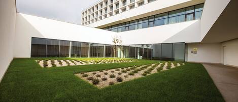 Un edificio moderno con un patio que presenta diseños geométricos en el césped y una escultura central.