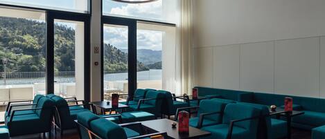 Un área de estar moderna con asientos color turquesa, ventanas amplias que ofrecen vista a un paisaje montañoso y una lámpara colgante de diseño contemporáneo.