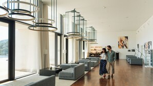 A modern hotel lobby with grey sofas, a wooden floor, and a large window offering a view. - Douro Royal Valley Hotel & SPA (Baiao)