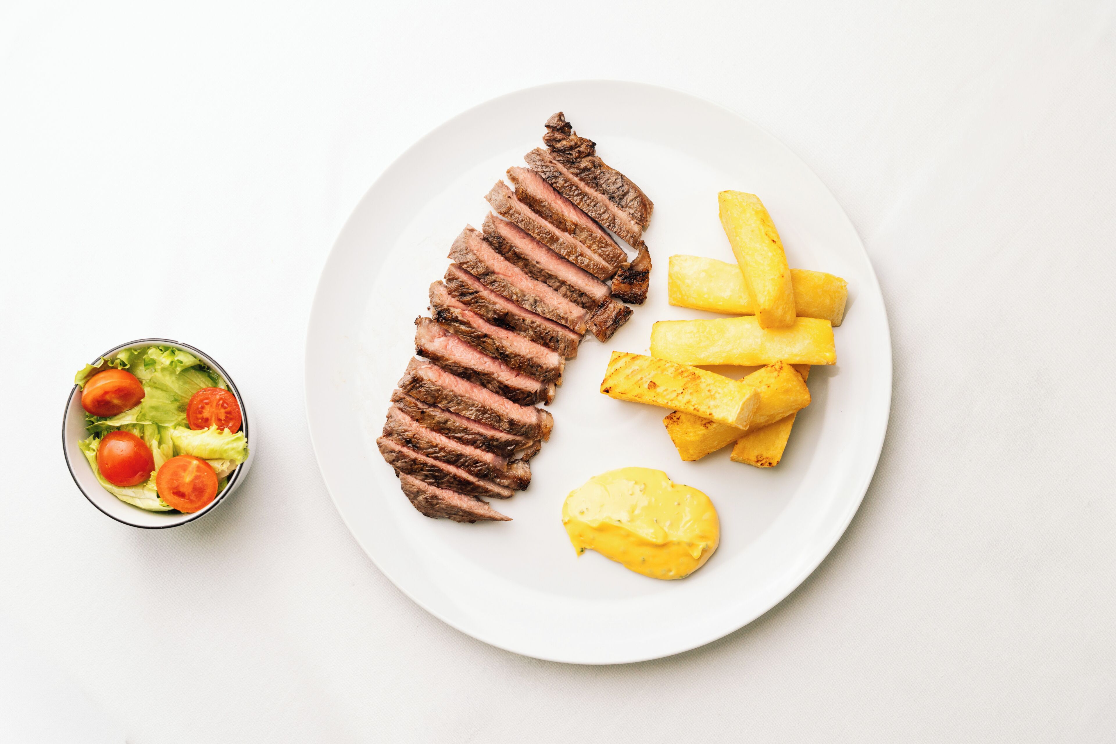 A plate with sliced steak, fries, and a small salad.