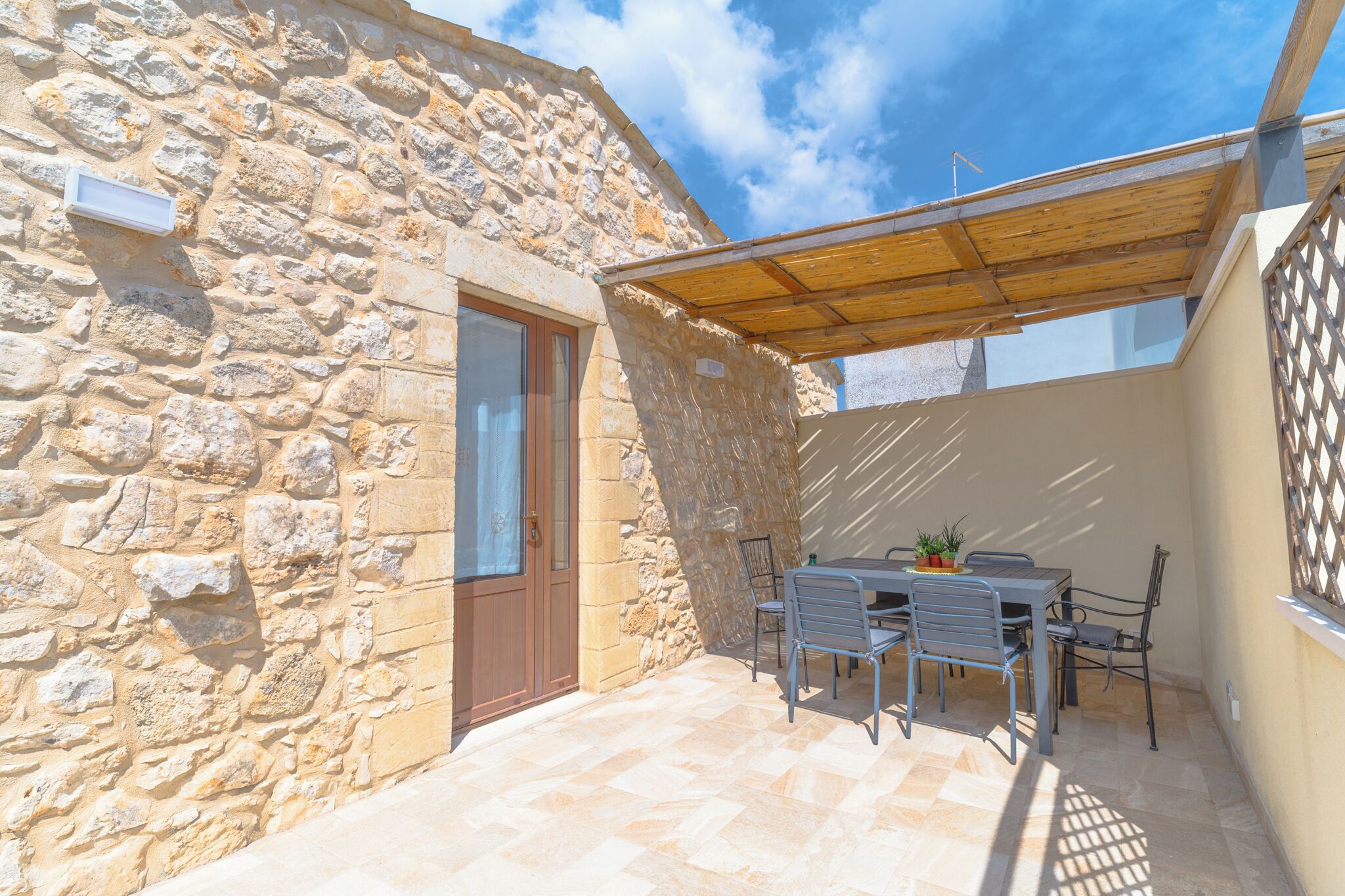 Un edificio de piedra con puerta de madera, un patio cubierto con mesa y sillas, y vista al cielo.