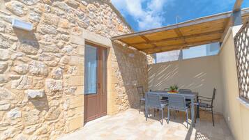 Un edificio de piedra con puerta de madera, un patio cubierto con mesa y sillas, y vista al cielo.