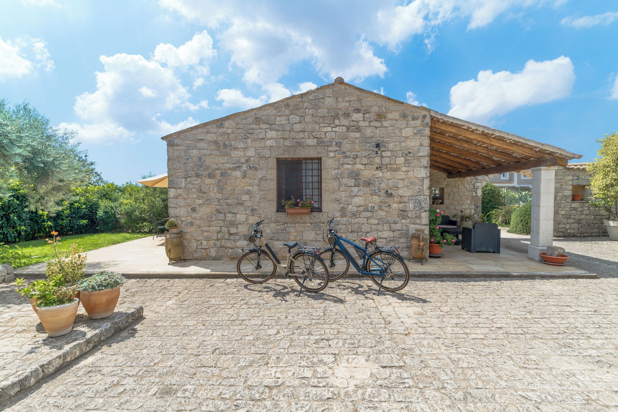 Un bâtiment en pierre avec un toit en bois, un vélo garé devant et des plantes en pot.